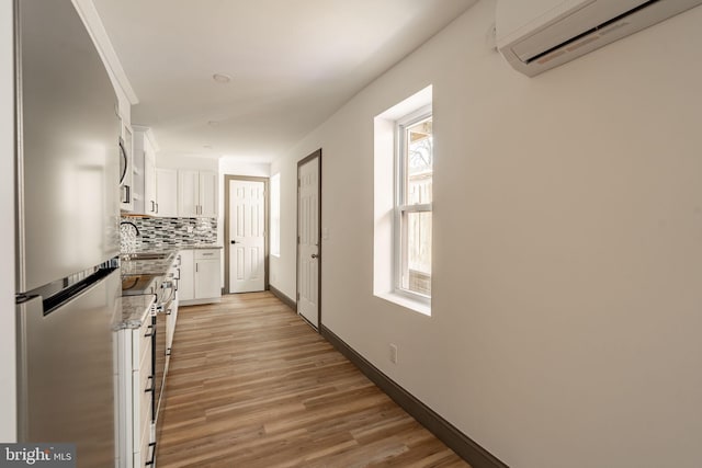 hallway with a sink, light wood-type flooring, baseboards, and a wall unit AC