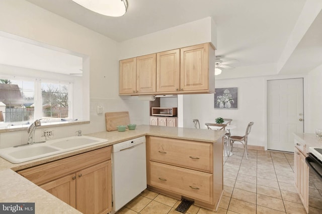 kitchen with light countertops, light brown cabinets, white dishwasher, and a sink