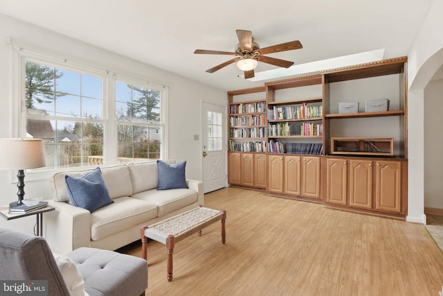 sitting room featuring light wood-style flooring, a ceiling fan, arched walkways, and baseboards