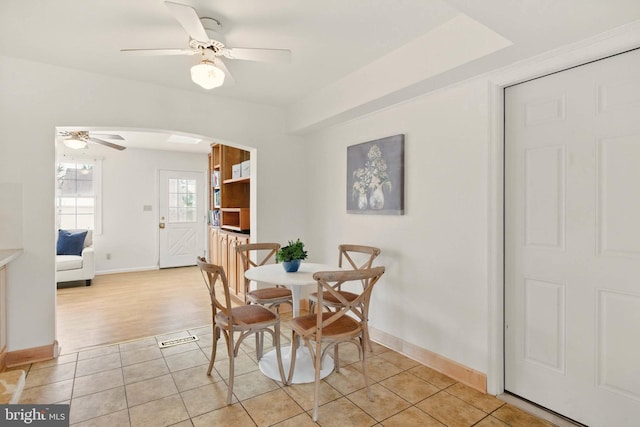 dining room featuring light tile patterned floors, a ceiling fan, arched walkways, and baseboards