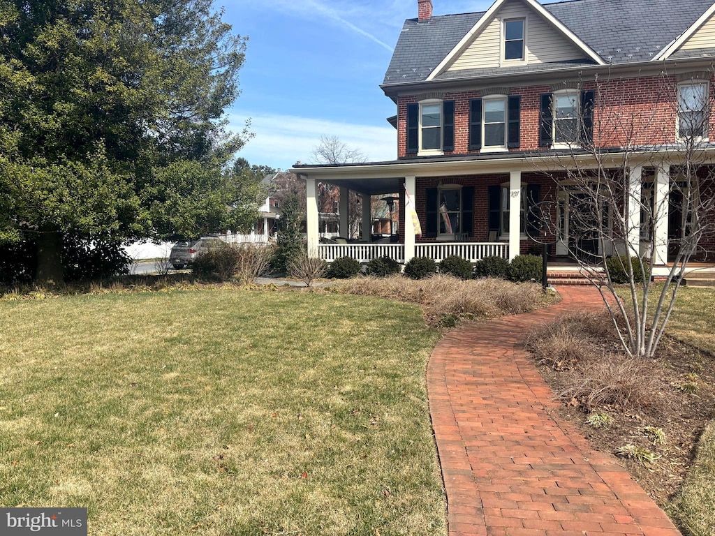 view of front of house with a chimney, brick siding, a porch, and a front yard