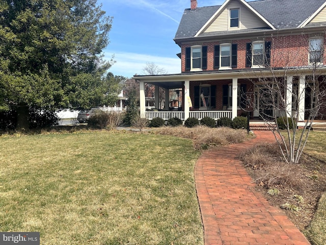 view of front of home with a chimney, brick siding, a porch, and a front lawn