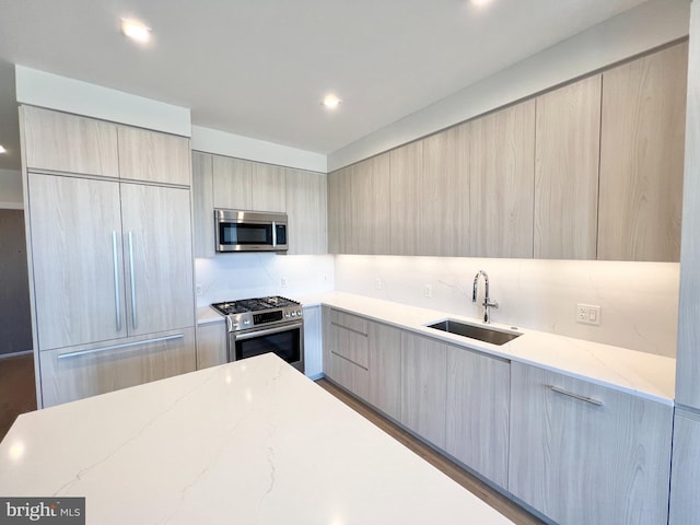 kitchen featuring backsplash, light stone countertops, appliances with stainless steel finishes, modern cabinets, and a sink