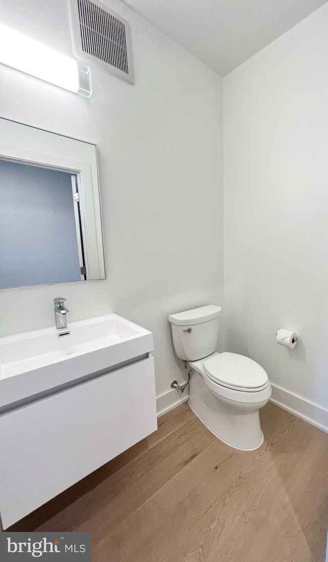 bathroom featuring vanity, wood finished floors, visible vents, baseboards, and toilet