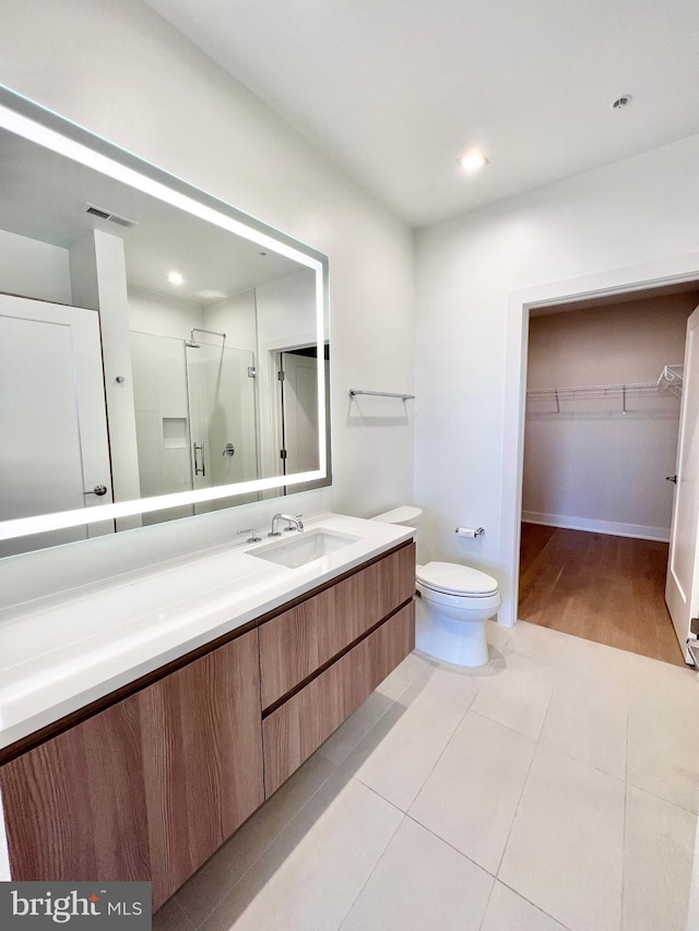 bathroom with vanity, a shower stall, a walk in closet, tile patterned floors, and toilet