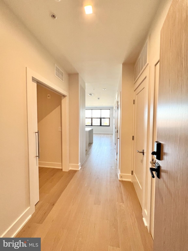 hallway with baseboards, visible vents, and light wood-type flooring