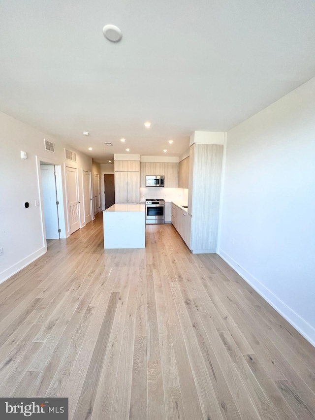 kitchen featuring baseboards, light countertops, appliances with stainless steel finishes, light wood-type flooring, and a center island