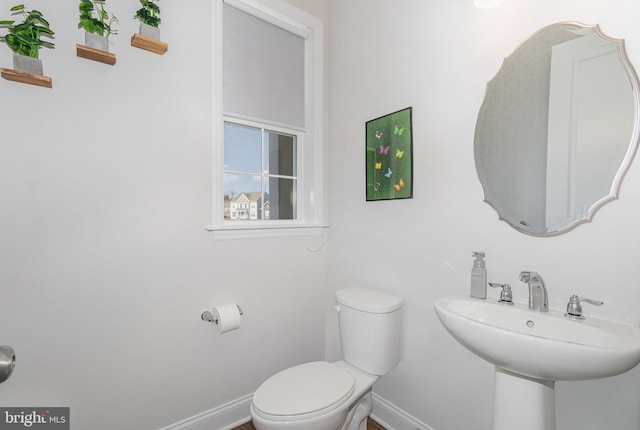 half bath featuring toilet, baseboards, and a sink