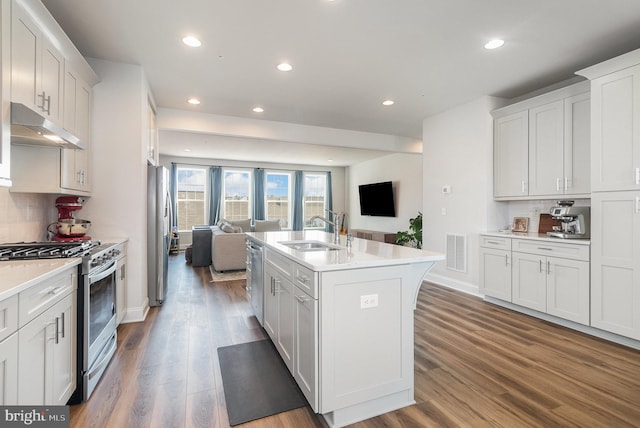 kitchen with visible vents, under cabinet range hood, open floor plan, stainless steel appliances, and a sink