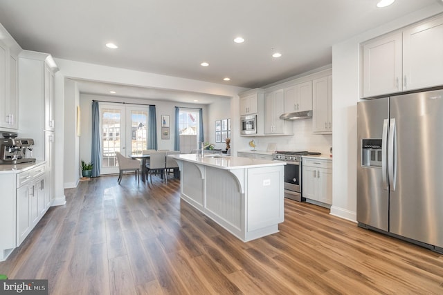 kitchen with tasteful backsplash, under cabinet range hood, light countertops, appliances with stainless steel finishes, and wood finished floors