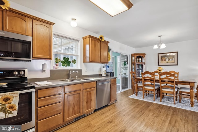 kitchen featuring light wood finished floors, a sink, appliances with stainless steel finishes, brown cabinets, and a chandelier