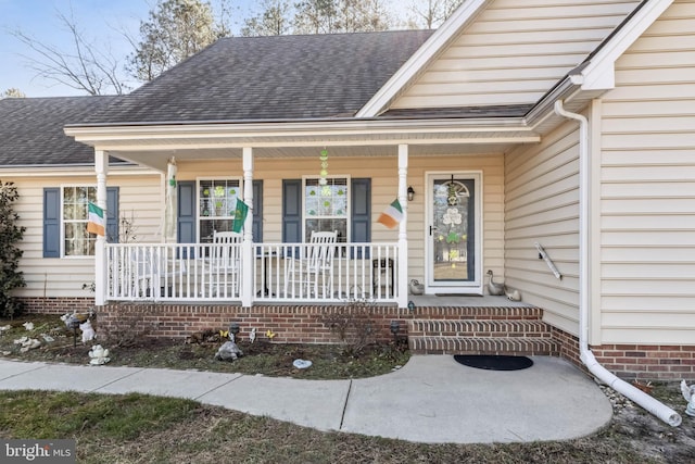 view of exterior entry featuring covered porch and a shingled roof