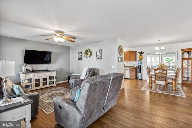 living room featuring ceiling fan with notable chandelier, wood finished floors, and baseboards