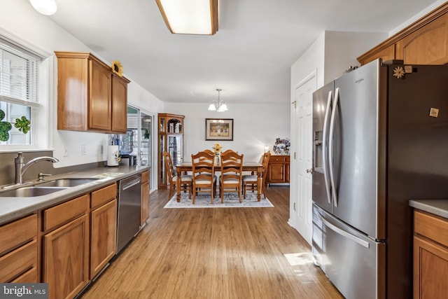 kitchen with brown cabinetry, light wood-style floors, appliances with stainless steel finishes, and a sink