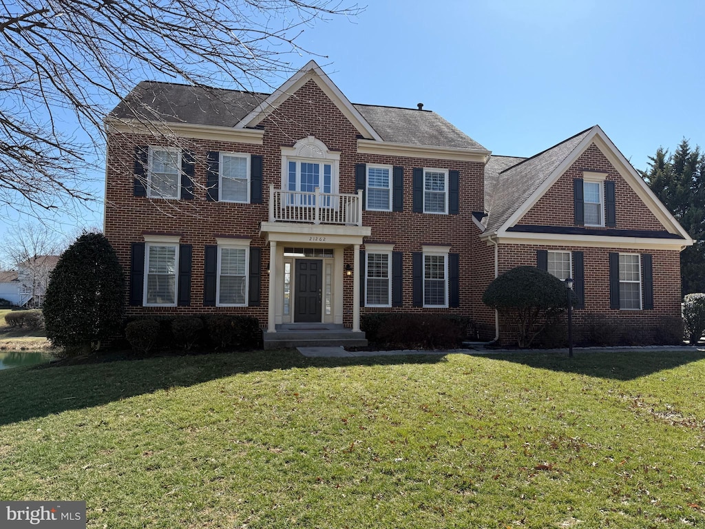 colonial inspired home with brick siding, a front yard, and a balcony