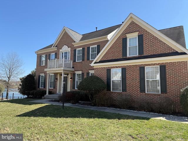 colonial home featuring a front yard, a balcony, and brick siding