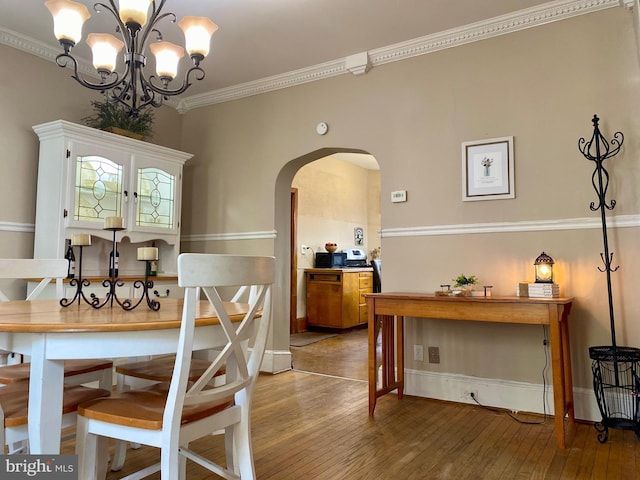 dining space with arched walkways, an inviting chandelier, hardwood / wood-style floors, and crown molding