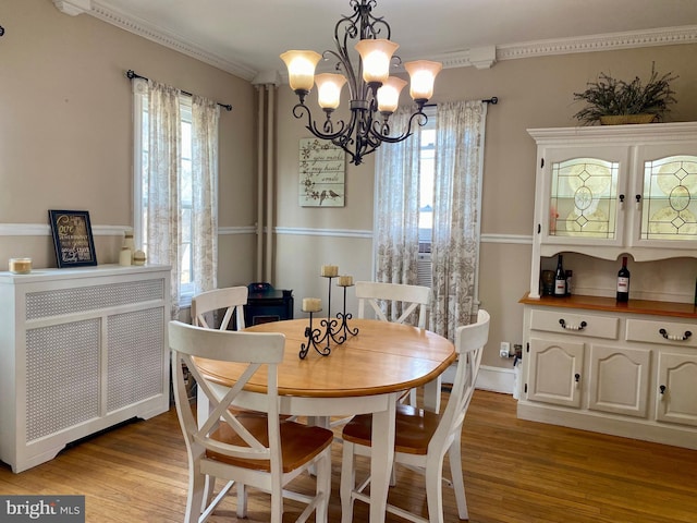 dining area featuring light wood-type flooring, radiator, a chandelier, and crown molding