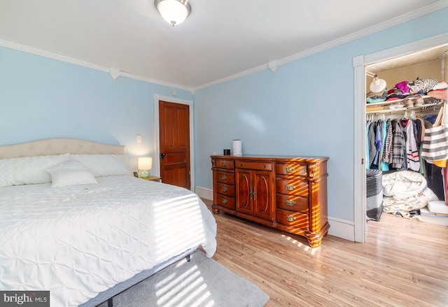 bedroom with a closet, wood finished floors, a spacious closet, and ornamental molding