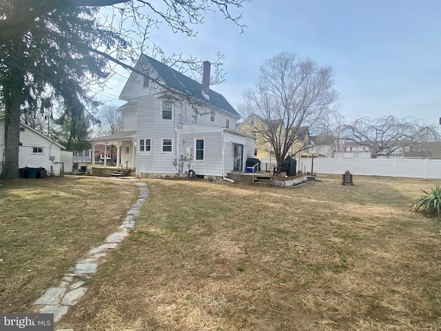 rear view of property featuring a lawn, a chimney, and fence