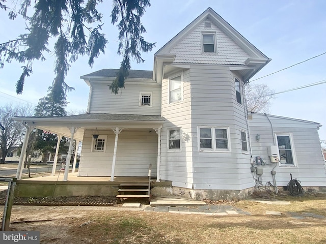 rear view of property with covered porch and roof with shingles