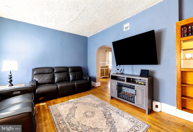 living area with arched walkways, a textured ceiling, baseboards, and hardwood / wood-style floors