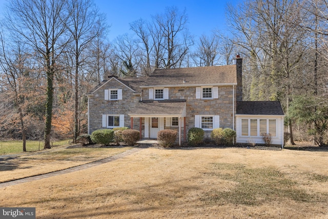 view of front of house with a front yard, stone siding, and a chimney