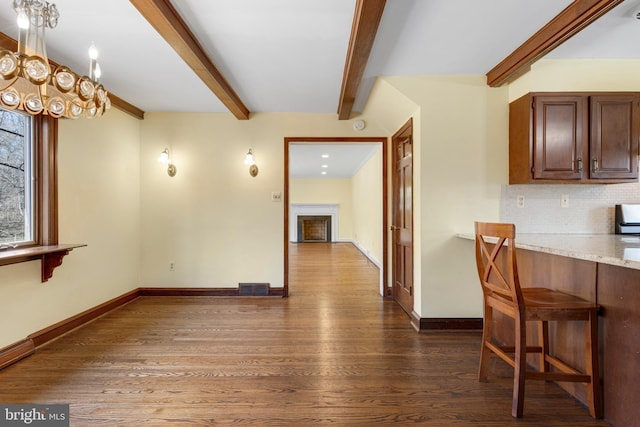 dining area featuring baseboards, beam ceiling, dark wood finished floors, and a fireplace