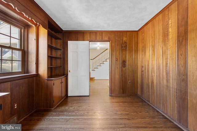 spare room with stairs, built in shelves, wood finished floors, and wood walls