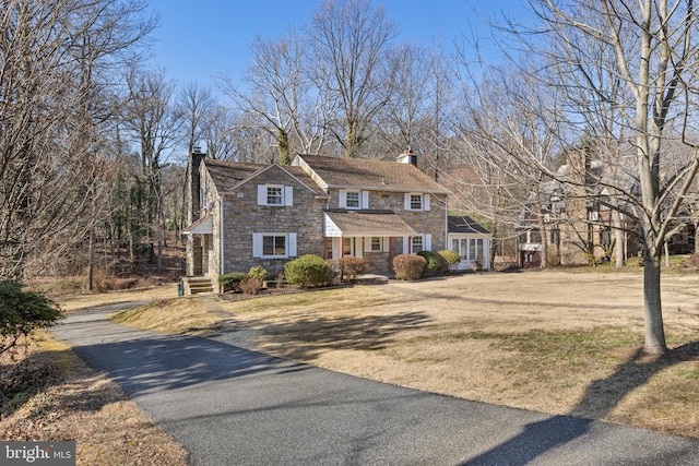 view of front of house with stone siding, a front lawn, and a chimney