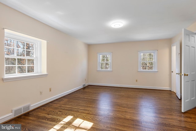 spare room with wood finished floors, visible vents, and baseboards