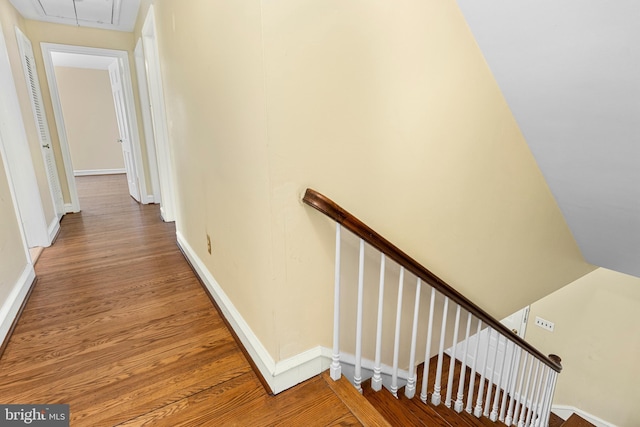 corridor featuring baseboards, an upstairs landing, attic access, and wood finished floors