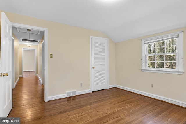 empty room featuring wood finished floors, visible vents, baseboards, attic access, and vaulted ceiling