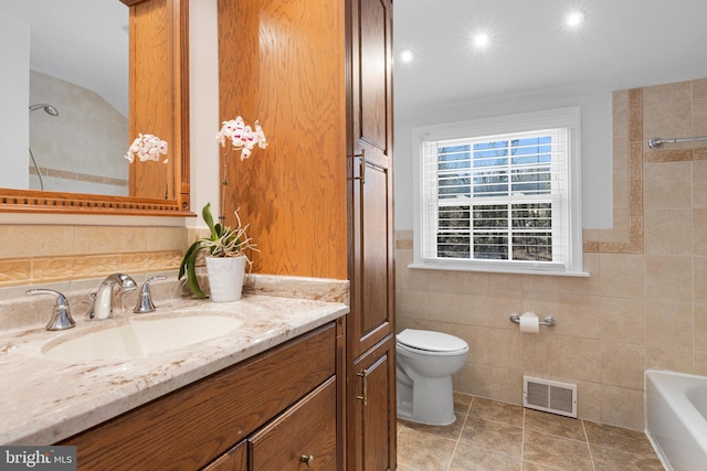 bathroom featuring visible vents, toilet, a bathing tub, tile walls, and vanity