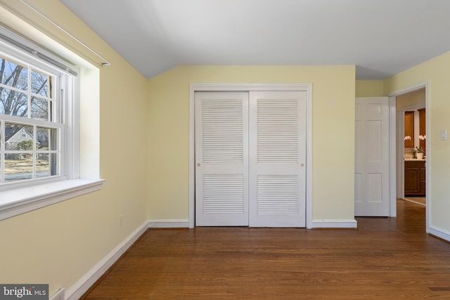 unfurnished bedroom with a closet, lofted ceiling, baseboards, and wood finished floors