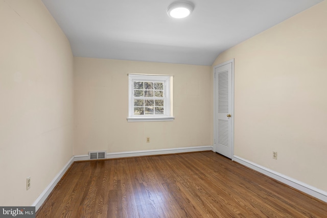 spare room featuring vaulted ceiling, wood finished floors, visible vents, and baseboards