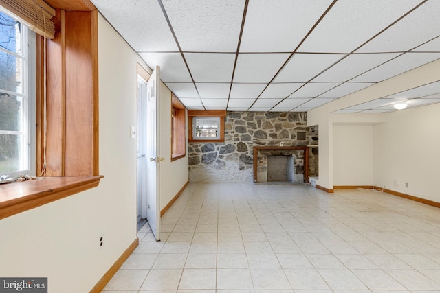 unfurnished living room with light tile patterned floors, a drop ceiling, a fireplace, and baseboards