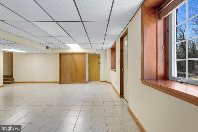 basement with light tile patterned flooring, stairs, a paneled ceiling, and baseboards