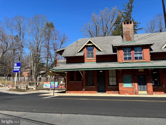 view of property with brick siding, a porch, and a chimney