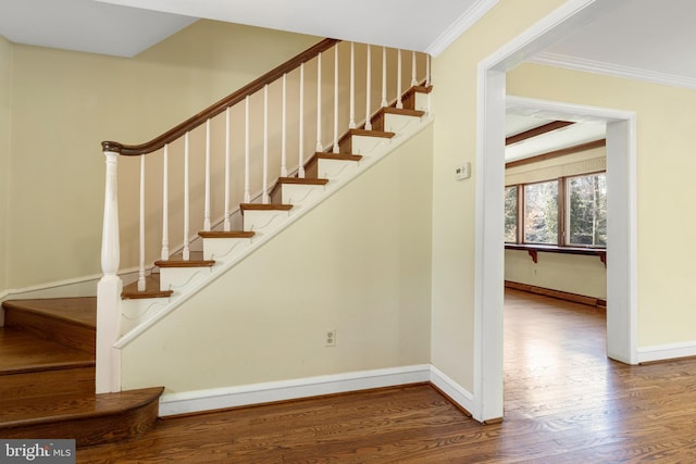 stairway with wood finished floors, baseboards, and ornamental molding