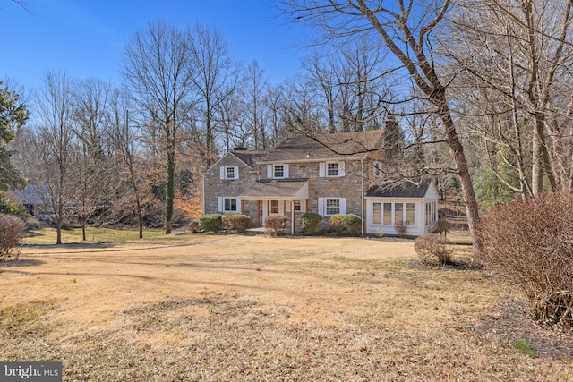 shingle-style home featuring stone siding, a front lawn, and a chimney