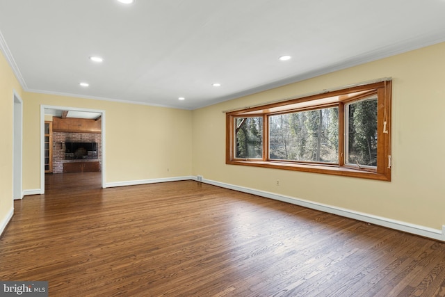 spare room featuring baseboards, a brick fireplace, wood finished floors, and crown molding