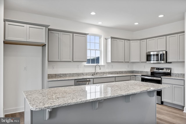 kitchen featuring gray cabinetry, a sink, a kitchen breakfast bar, wood finished floors, and appliances with stainless steel finishes