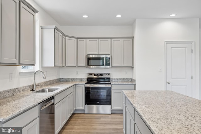 kitchen with a sink, stainless steel appliances, gray cabinets, and light wood finished floors