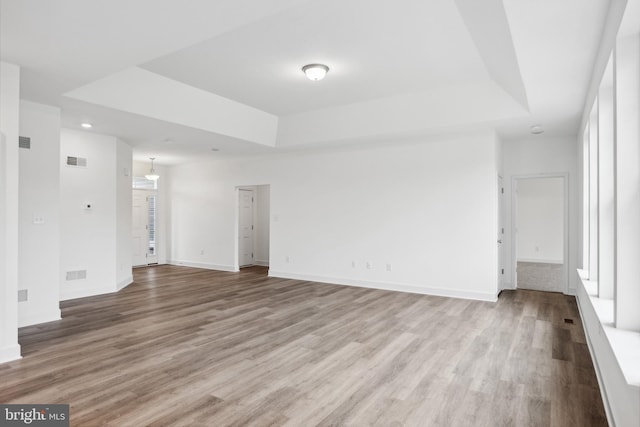 empty room with a tray ceiling, wood finished floors, and visible vents