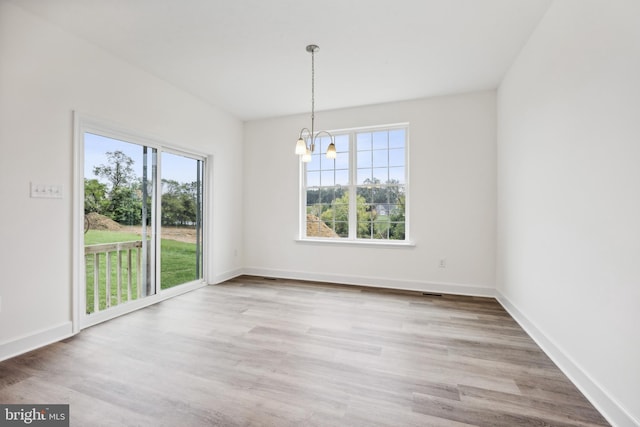 unfurnished dining area featuring a wealth of natural light, a notable chandelier, baseboards, and wood finished floors