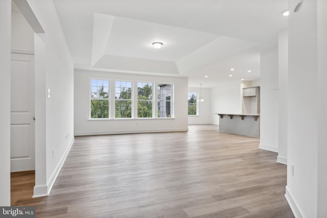 unfurnished living room with a tray ceiling, recessed lighting, light wood-style floors, and baseboards