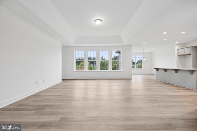 unfurnished living room featuring a tray ceiling, recessed lighting, baseboards, and light wood finished floors