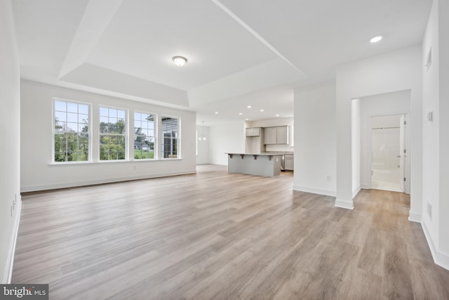 unfurnished living room featuring recessed lighting, baseboards, light wood-type flooring, and a tray ceiling