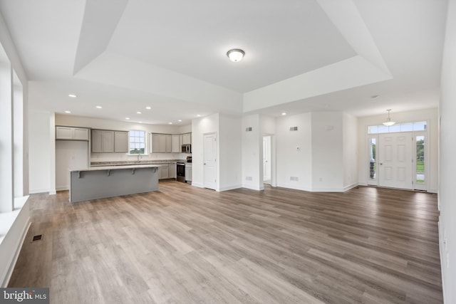 unfurnished living room featuring recessed lighting, a tray ceiling, baseboards, and light wood-style flooring